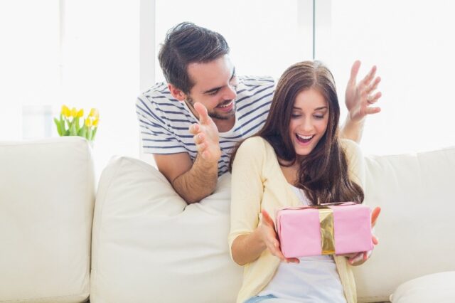 A surprised woman receives a beautifully packaged gift from her partner, illustrating the emotional impact of custom boxes and packaging, highlighting how thoughtful packaging can enhance the unboxing experience and strengthen brand connections.